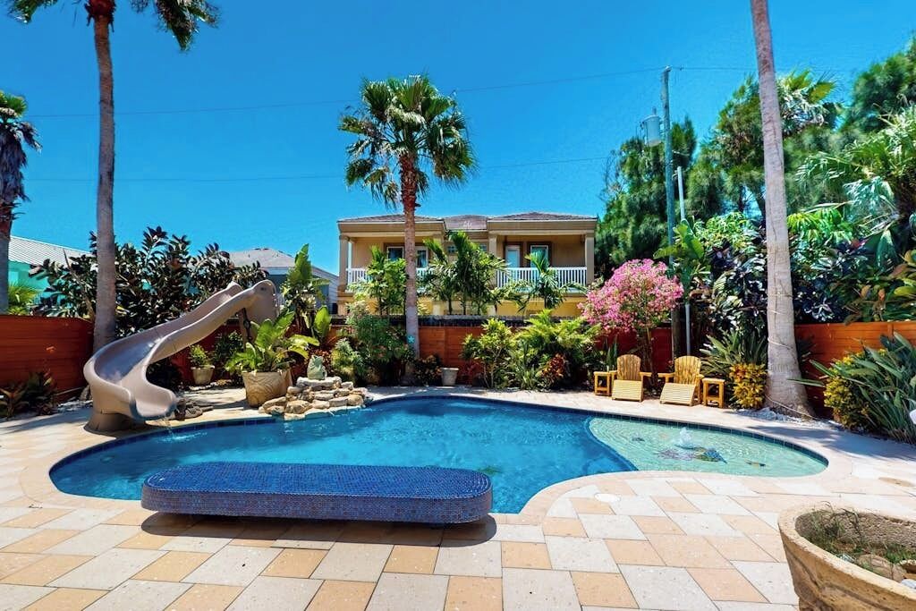 Una piscina con uno scivolo, circondata da palme e diverse piante.