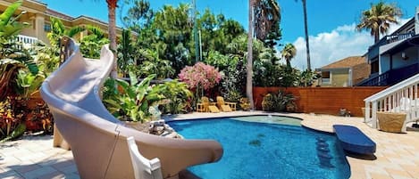 Una piscina amb tobogan, envoltada d'arbres de palmera i una tanca de fusta.