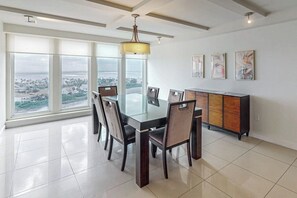 Un comedor moderno con una mesa de vidrio, sillas y vistas de la ciudad a través de amplios ventanales.