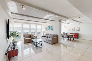 A spacious living area with a large window, a sofa, a coffee table, and a dining set. - Solare Tower 1202 - Gulf Views & Beach Access (South Padre Island)