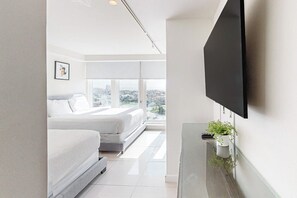 A modern hotel room with a bed, a television mounted on the wall, and a city view. - Solare Tower 1202 - Gulf Views & Beach Access (South Padre Island)