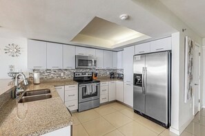 A modern kitchen with white cabinets, stainless steel appliances, and a tiled backsplash. - Solare Tower 1202 - Gulf Views & Beach Access (South Padre Island)