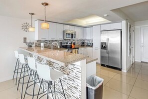A modern kitchen with a central island, bar stools, stainless steel appliances, and pendant lighting. - Solare Tower 1202 - Gulf Views & Beach Access (South Padre Island)