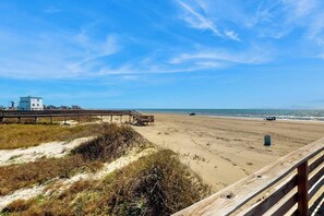 Ein Strand mit einem hölzernen Steg, Sanddünen und einem klaren Himmel.