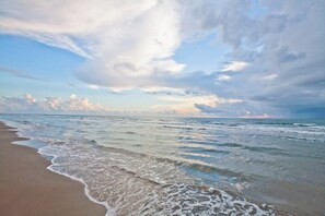 A beach with waves gently lapping onto the shore under a partly cloudy sky. - La Internacional Condominiums #202 (South Padre Island)