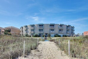 A beachfront apartment building with a central entrance, multiple balconies, and a sandy pathway leading to the entrance. - La Internacional Condominiums #202 (South Padre Island)