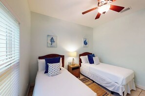 Ein Hotelzimmer mit zwei Betten, einem Deckenventilator und Bildern an den Wänden.