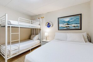 Una habitación con literas, un cuadro de un faro, un reloj y una lámpara de noche.