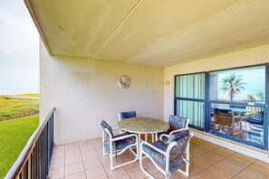 Ein Balkon mit rundem Tisch und Stühlen, Blick aufs Meer und eine durch das Fenster sichtbare Palme.