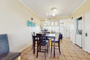 A dining area with a table and chairs, a kitchen in the background, and a ceiling fan. - Dolphin Condominiums #20 (South Padre Island)
