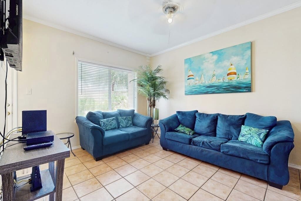Ein Wohnzimmer mit zwei blauen Sofas, einem Fernseher auf einem Schrank und einem Bild von Segelbooten an der Wand.