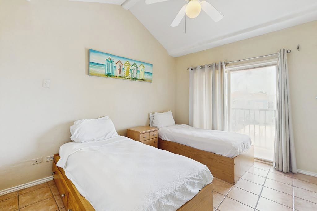 Een slaapkamer met twee bedden, een plafondventilator, een raam met gordijnen en een schilderij aan de muur.