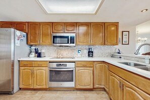 A kitchen with wooden cabinets, stainless steel appliances, a microwave, and a coffee maker. - Suntide II Condominiums #306 (South Padre Island)