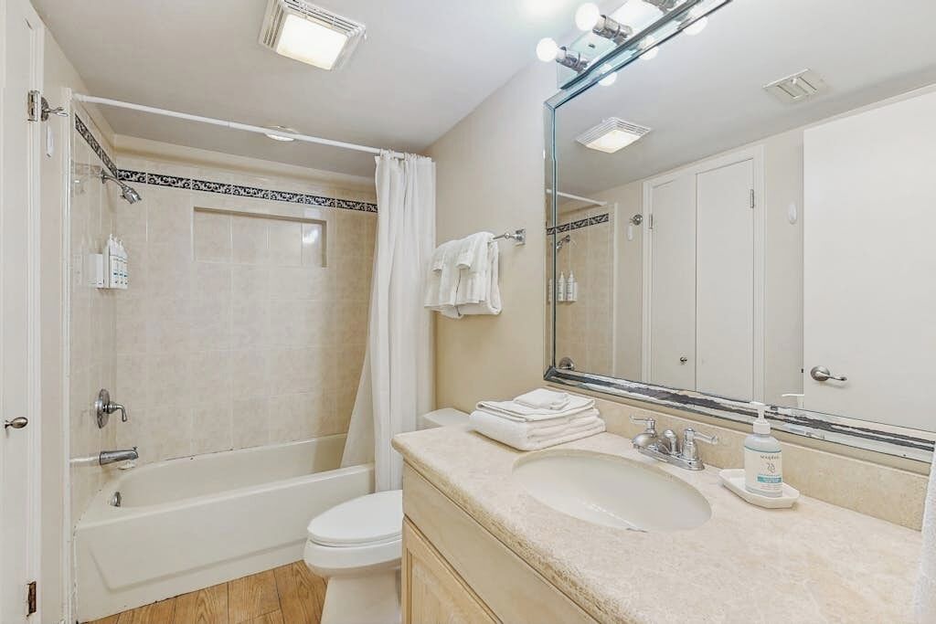 A bathroom with a bathtub, toilet, sink, and a large mirror.