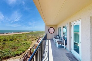 A balcony with a view of the beach, a circular wall decoration, and a row of white chairs. - Suntide II Condominiums #306 (South Padre Island)