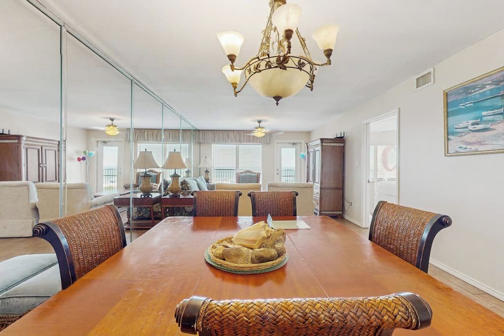 A dining room with a wooden table, woven chairs, and a chandelier.