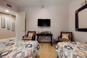 A hotel room with two beds, a television mounted on the wall, a small table with a lamp, and a trash bin. - Sapphire Condominiums #603 (South Padre Island)