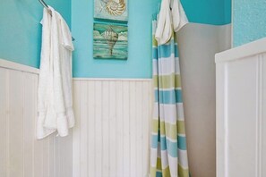 A bathroom with a blue wall, white shower curtain, and a white towel hanging on a rack. - Saltwater Dreams - Second Row, Steps to the Sand (Galveston)