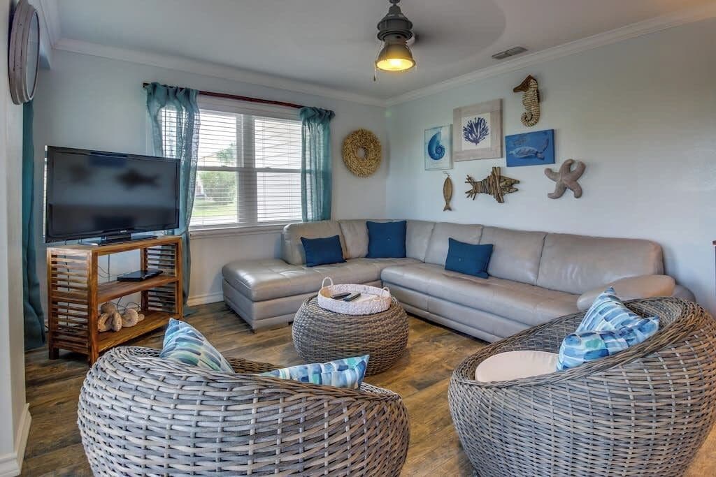 Ein Wohnzimmer mit einer Couch, zwei Korbstühlen, einem Fernseher auf einem Holzständer und Wanddekoration.