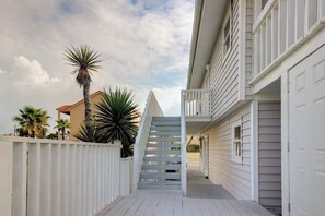 A narrow pathway leading to a white building with a balcony, surrounded by palm trees and a white fence. - Mezquite House - Ocean Views, Sleeps 16, Dogs OK (South Padre Island)