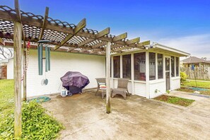 A covered patio with a grill, chairs, and a wooden pergola. - Birder's Heaven at 621 Palm (Laguna Vista)