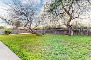 A backyard with a wooden fence, a tree, and a grassy lawn. - Birder's Heaven at 621 Palm (Laguna Vista)
