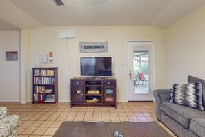 A living room with a television, bookshelf, and a sofa. - Birder's Heaven at 621 Palm (Laguna Vista)