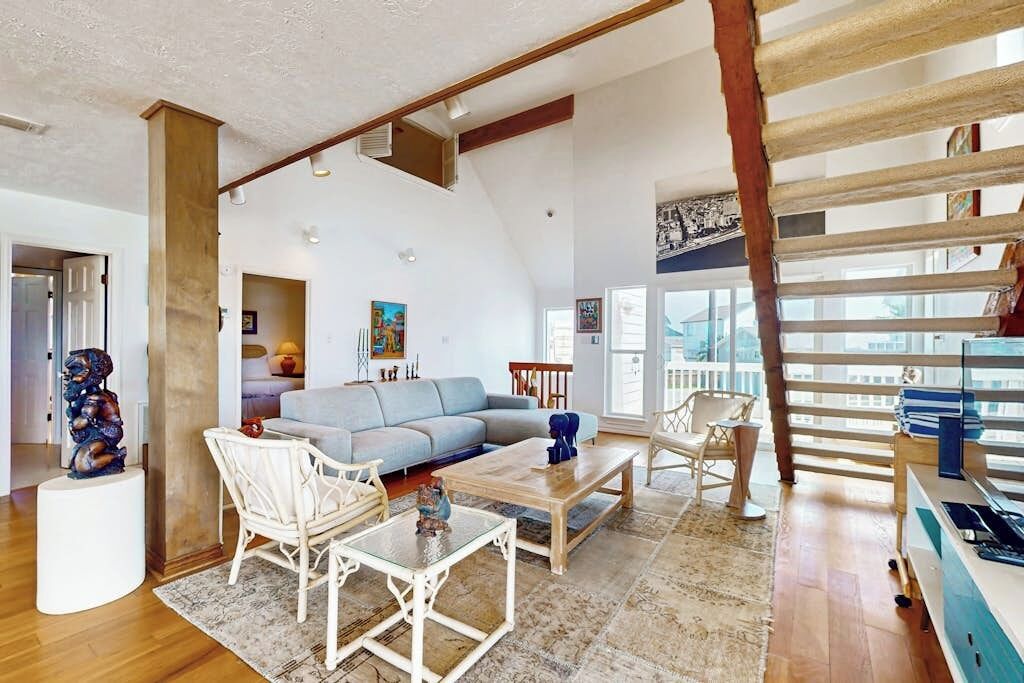 Un salon spacieux avec un plafond haut, un canapé, une table basse et un coin repas avec des chaises.