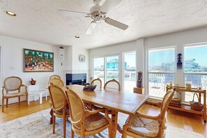 A spacious dining area with a large wooden table and wicker chairs, a ceiling fan, and a painting on the wall. - Mon Repose - Bayfront Home with Big Deck (Jamaica Beach)