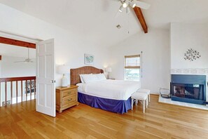 A bedroom with a bed, bedside tables, a dresser, a window, a fireplace, and a ceiling fan. - Mon Repose - Bayfront Home with Big Deck (Jamaica Beach)