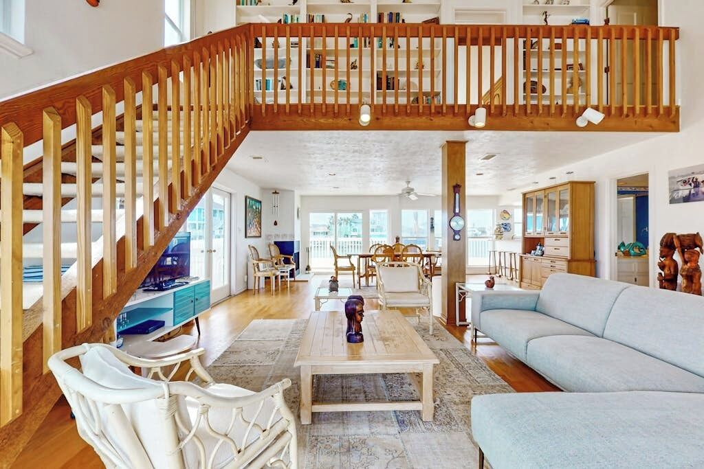 A spacious living area with a wooden staircase, a light blue sofa, and a dining area with chairs and a table.