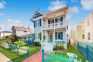 A two-story house with a front porch, a small front yard, and a blue fence. - Blue Sky Getaway - Private Pool & Historic Charm (Galveston)