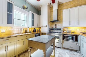 A kitchen with white cabinets, a granite countertop, stainless steel appliances, and a hanging light fixture. - Blue Sky Getaway - Private Pool & Historic Charm (Galveston)