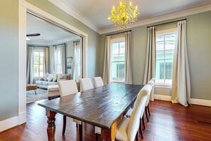 A dining room with a long wooden table, white chairs, and a chandelier. - Blue Sky Getaway - Private Pool & Historic Charm (Galveston)