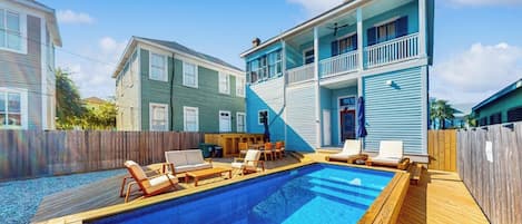 Une propriété résidentielle dotée d’une piscine, d’une terrasse en bois et d’une maison à deux étages avec un balcon.