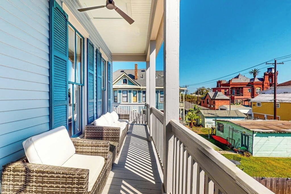 A covered porch with wicker furniture, a ceiling fan, and a view of neighboring houses.