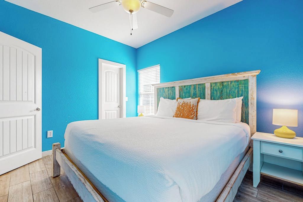 A bedroom with a bed, a nightstand, a ceiling fan, and a door.
