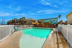 A rectangular swimming pool with a white fence, a wooden deck, and a clear blue sky. - The Coral Cove - Walk to Beach, Pool & Dogs OK (Port Aransas)