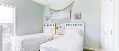 A room with two beds, a ceiling fan, a window, and artwork on the wall.