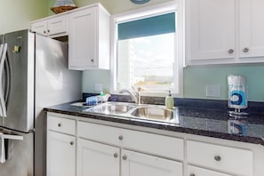 A kitchen with white cabinets, a stainless steel refrigerator, a double sink, and a window with a view. - Las Joyas Bayview Home 104 (Port Isabel)