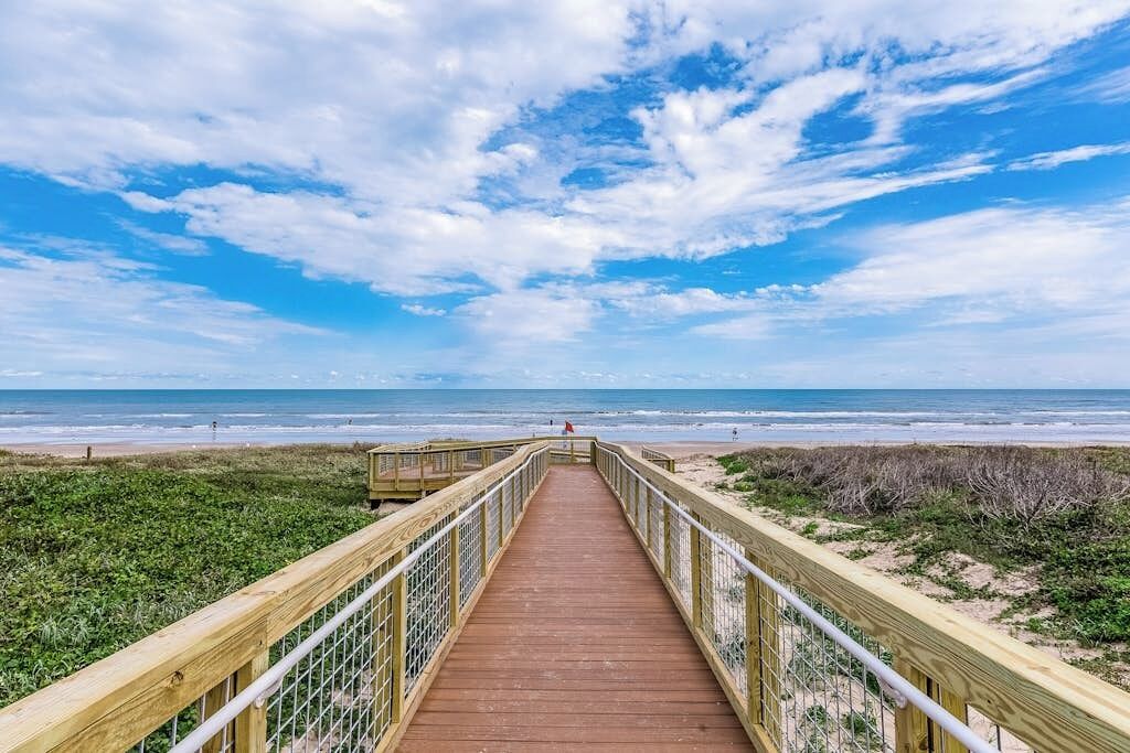 A wooden boardwalk leading to a beach with a clear sky.