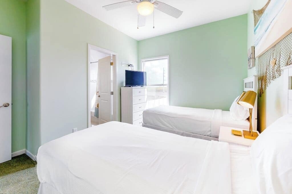 Une chambre d’hôtel avec deux lits, une télévision, un bureau avec une lampe et un ventilateur de plafond.