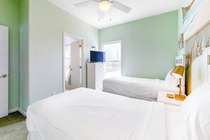 Ein Hotelzimmer mit zwei Betten, einem Fernseher, einem Schreibtisch mit Lampe und einem Deckenventilator.