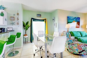 Ein modernes Wohnzimmer mit einem Glastisch, grünen Stühlen, einer floralen Couch und einem Gemälde an der Wand.