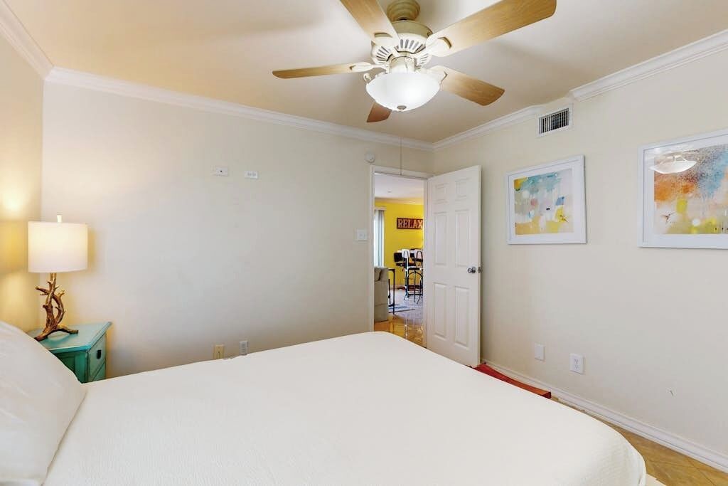 A bedroom with a bed, a ceiling fan, a nightstand, and a door leading to another room.