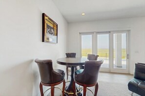 A dining area with a round table and two chairs, a framed picture on the wall, and a sliding glass door leading to a balcony. - Padre Villa 102 - Waterfront Dock, Walk to Beach (Corpus Christi)