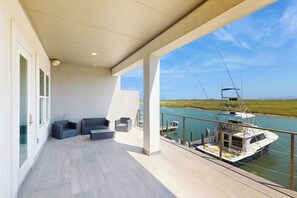 A balcony with a view of a river and a boat, featuring a seating area with cushions. - Padre Villa 104 - Gulf & Lake Views, Sleeps 14 (Corpus Christi)
