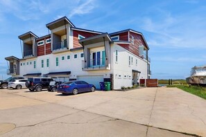 A multi-story residential building with a garage, a covered parking area, and a boat in the background. - Padre Villa 104 - Gulf & Lake Views, Sleeps 14 (Corpus Christi)
