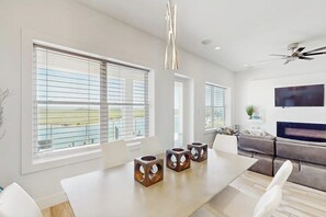 A modern living room with a large window, a flat-screen TV, and a ceiling fan. - Padre Villa 104 - Gulf & Lake Views, Sleeps 14 (Corpus Christi)