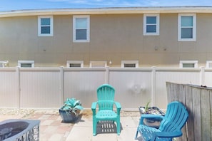A residential building with a beige exterior, a white fence, and two blue chairs in the backyard. - Sand Dollar #5 - Canal-Front, Pool & Pier (Corpus Christi)